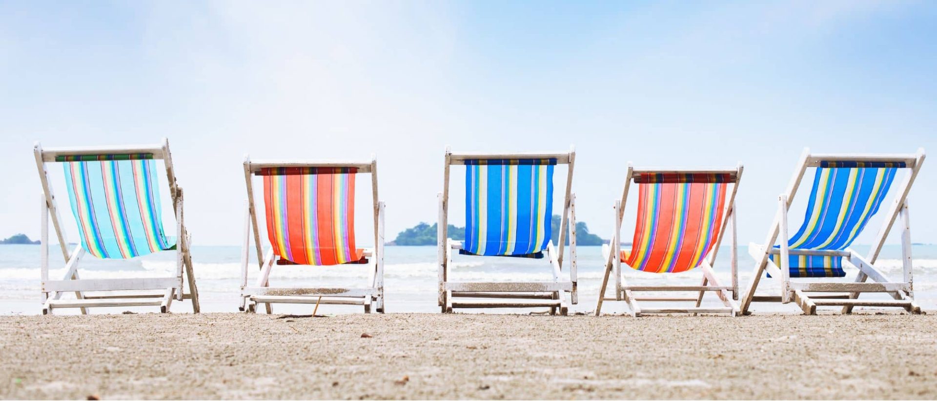 A row of colorful beach chairs on the sand.