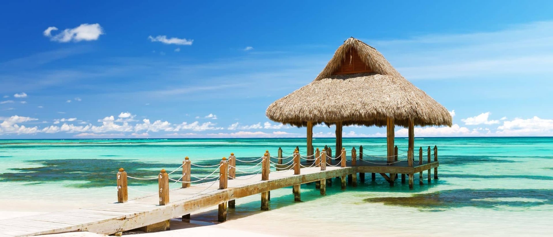 A wooden pier with a thatched roof on the beach.